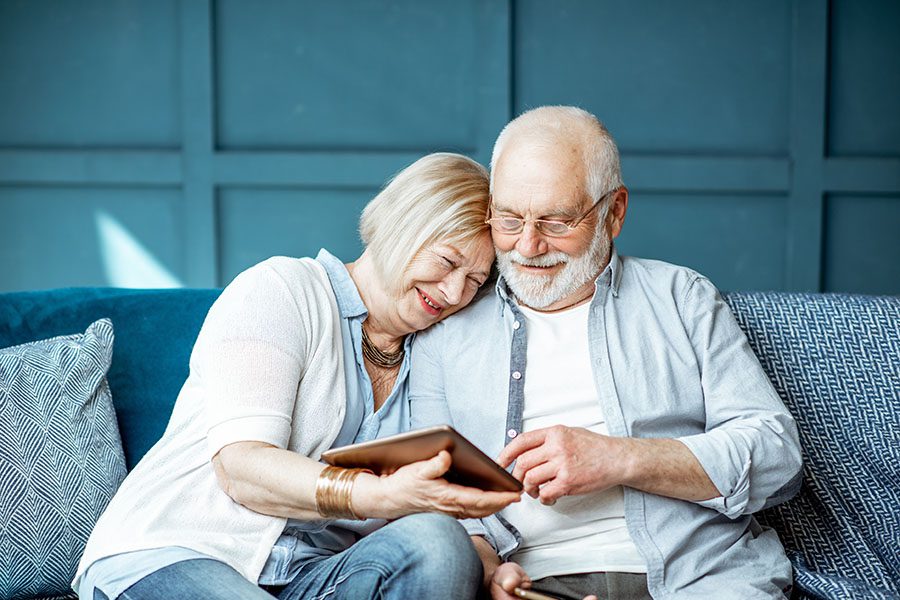 Client Center - Portrait of a Happy Mature Couple Sitting on the Sofa at Home While Using a Tablet Together
