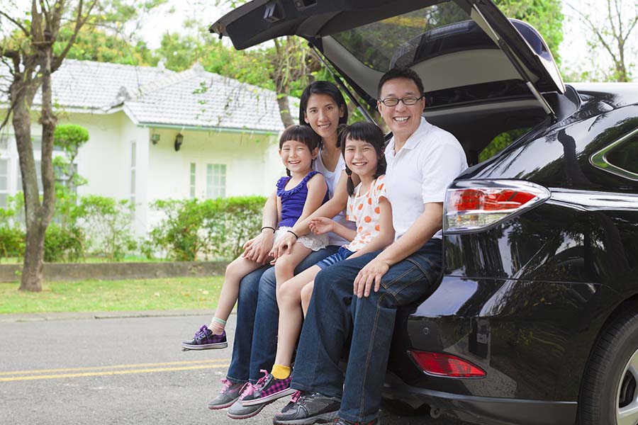 Personal Insurance - Happy Family with Two Kids Sitting in the Back Trunk of Their Car While Parked Next to Their House